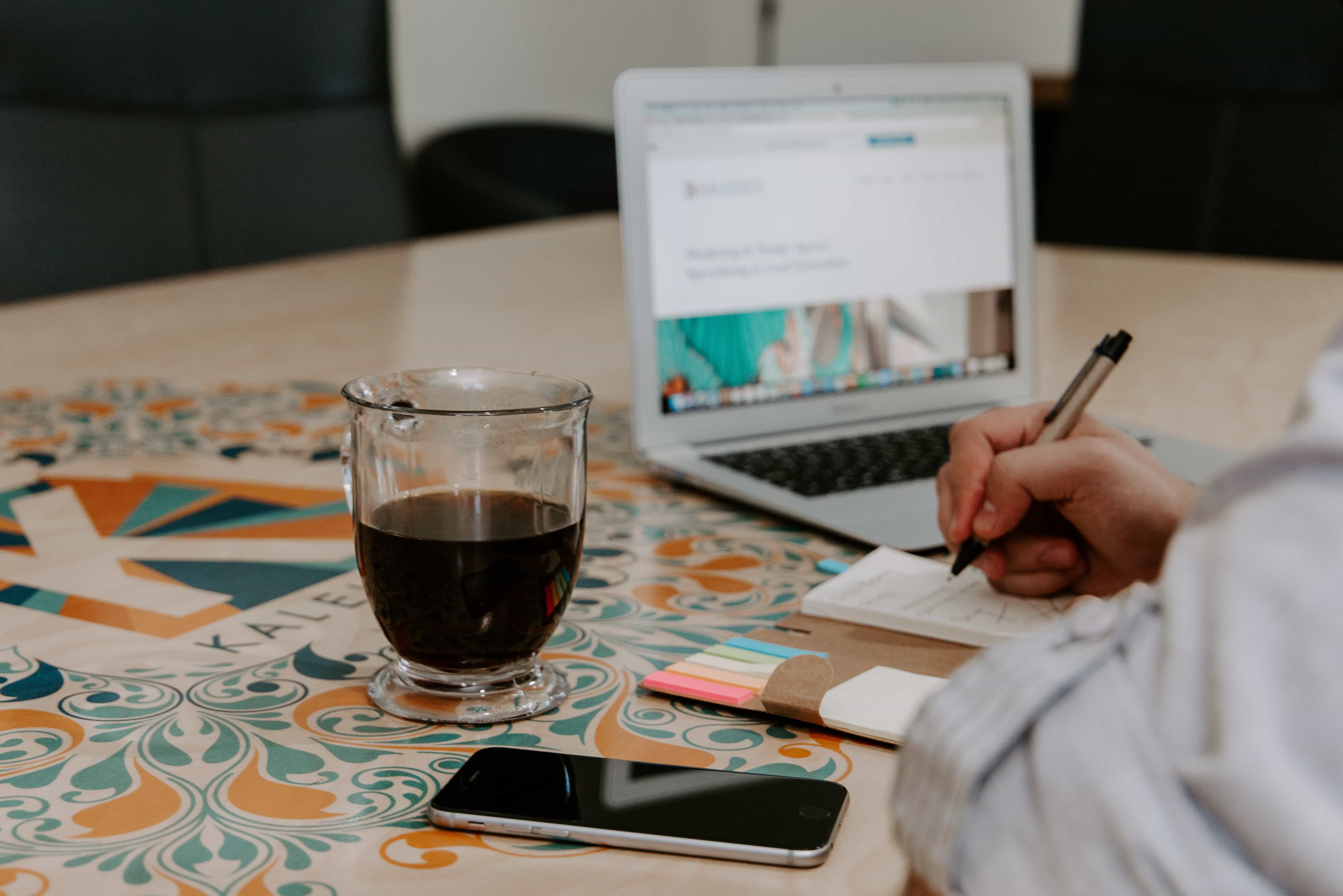 Person doing SEO analysis on a conference table with coffee, a notebook, and laptop